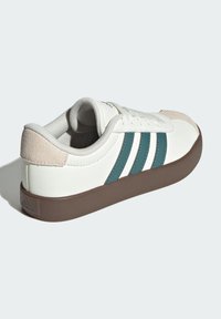 Biele kožené tenisky s tyrkysovými pruhmi, béžovými semišovými akcentmi a hnedou gumovou podrážkou. Majú okrúlu špičku a šnurovanie.