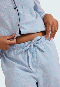 Ensemble de pyjama rayé bleu et blanc avec des motifs d'étoiles roses, comprenant un haut à boutons et un pantalon à taille élastique avec un nœud.