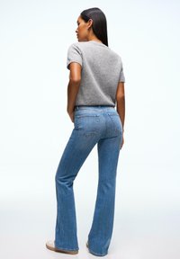 Pull gris clair à manches courtes associé à un jean bleu évasé, avec poches avant et arrière, taille mi-haute, et finition soignée.