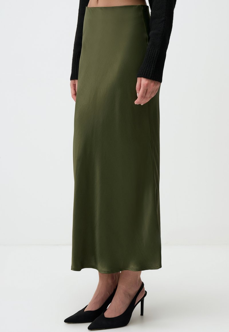 Olijfgroene satijnen maxi-rok met een gladde textuur en een subtiele glans, gecombineerd met zwarte spitse hakken.