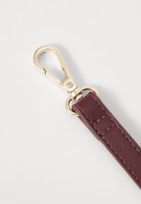Cinturino in pelle marrone con chiusura e anello dorati. Texture liscia con dettagli di cucitura visibili. Design compatto, adatto per accessori.