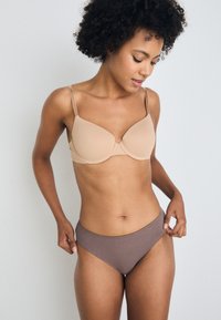 Beige draadloze bh met gladde cups en verstelbare bandjes, gecombineerd met bruine mid-rise slipjes, die een naadloze textuur tonen.