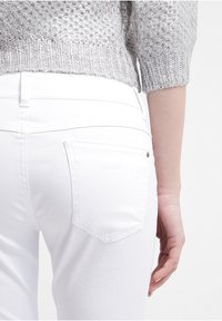 Jeans de mezclilla blanca con una silueta ajustada, que presentan un bolsillo trasero y costuras sutiles. Llevados con un suéter de punto texturizado en plata.