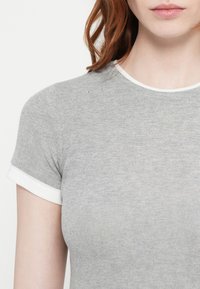 Grå ribbestrikket t-skjorte med korte ermer, som har hvit kant rundt kragen og ermåpningene. Glatt tekstur og tettsittende design.