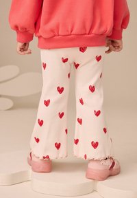 Kermarin ribbede flare-bukser med røde hjerte mønstre, parret med rosa sko med flæser; båret med en koralfarvet sweatshirt.