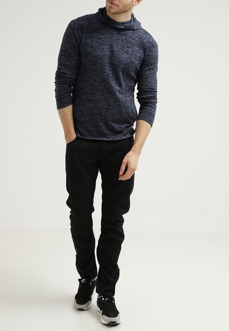 Marinblus, texturerad långärmad topp med krage, kombinerad med svarta byxor och träningsskor, stående mot en ljus bakgrund.
