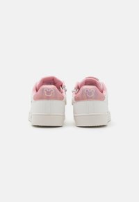 Vita sneakers med rosa accenter, med en glänsande, iridescent hälflik och en diskret Mickey Mouse-logotyp på baksidan. Slät textur.