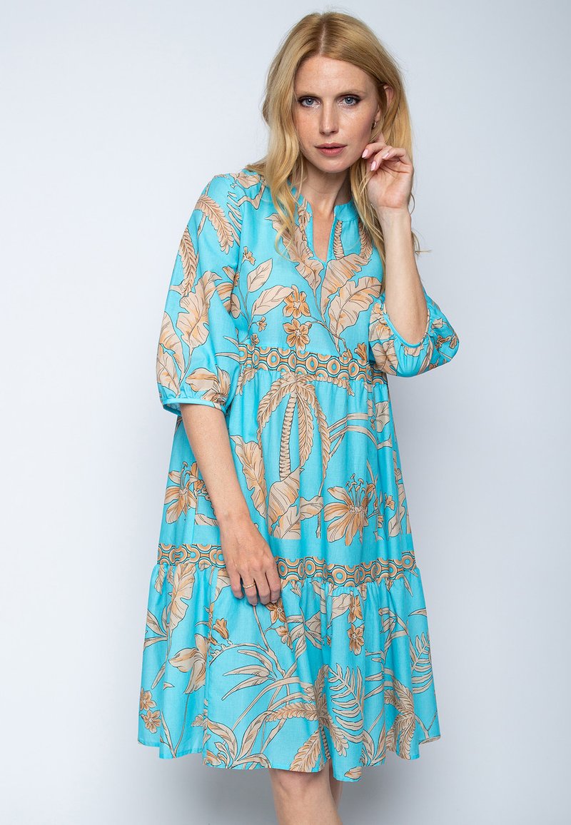 Blauwe bloemenjurk met beige tropische patronen, een relaxte pasvorm, knoopsluiting aan de hals en driekwartmouwen. Uitlopende onderkant.