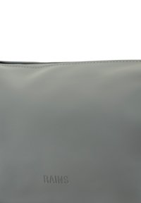 Borsa impermeabile grigia realizzata in materiale liscio. Presenta un design semplice con testo in rilievo, cuciture bianche lungo il bordo superiore, senza altri accenti.