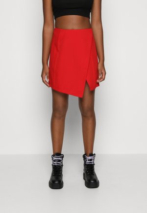 Rode wikkel-minirok met een gestructureerde afwerking, voorzien van een hoge taille en asymmetrische zoom. Gecombineerd met zwarte veterlaarzen met een grove zool.