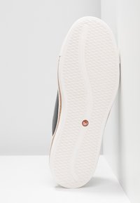 Basket noire avec un dessus texturé gris, une semelle en caoutchouc blanche avec un motif de bande de roulement, et un détail de logo rouge.