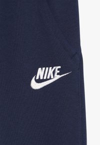 Marinblå bomullsmjukisbyxor med en vit broderad Nike-logotyp och en krökt swoosh-design på vänster fickområde.