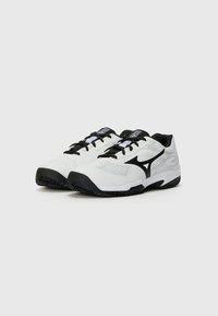 White athletic shoes with black accents, mesh and synthetic upper, flat black rubber sole, and a textured pattern on the outsole.
