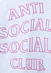Jasnoszary sweter z wyraźnym różowym haftem, na którym widnieje napis "ANTI SOCIAL SOCIAL CLUB", o miękkiej i gładkiej fakturze.