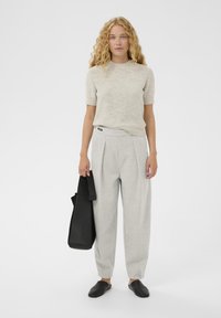 Világos bézs, rövid ujjú kötött pulóver, szürke pliszírozott nadrág és fekete bőr slip-on cipő. Fekete táska a bal kézben.