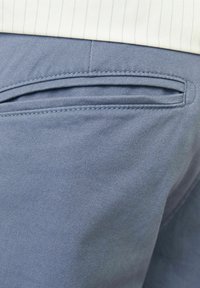 Pantalones de color azul claro presentan un bolsillo plano con costuras estrechas, una textura suave y un acabado de tela blanda. El diseño es sencillo y funcional.