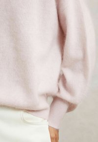 Maglione a maglia fuzzy rosa chiaro con maniche ampie e bordo, dal taglio morbido. Abbinato a jeans bianchi per creare contrasto.
