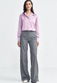 R óżowa satynowa koszula z długim rękawem i kołnierzykiem, zapinana na guziki, w połączeniu z szarymi spodniami w paski o szerokich nogawkach i białymi sneakersami.