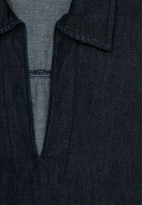 Dunkelblauses Denim-Hemd mit leicht offenem Kragen und scharfem V-Ausschnitt, sichtbaren Nähten und glatter Textur.