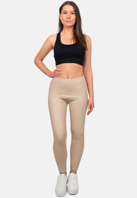 Top sportivo nero, leggings beige a vita alta, texture liscia, design aderente, abbinati a sneakers bianche.