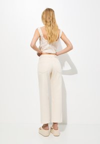 Top corto beige con diseño texturizado, combinado con pantalones cremosos de pierna ancha y cintura alta. Sandalias de plataforma completan el look.