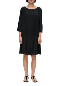 Svart plisserad klänning med rund halsringning och trekvartsärmar. Slät tyg med en flytande design, kombinerad med svarta sandaler.