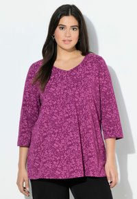 Haut magenta à manches trois-quarts, présentant un motif floral et un décolleté en V. Confectionné dans un tissu doux et texturé avec des plis.