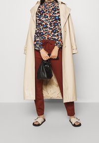 Beige trenčkot, vzorovaná halenka v modré, rezavé a hnědé barvě, rezavé kalhoty, černá taška na šňůrku a světlé sandály s přezkou.