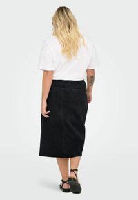 Črna denim midi krila s ravnim krojem, ki ima dve zadnji žep, v kombinaciji z ohlapno belo majico in črnimi sandalami.