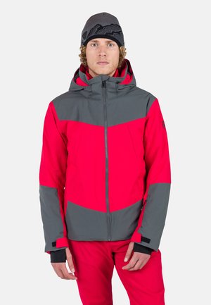Rote und graue Skijacke mit Reißverschluss, Kapuze und verstellbaren Bündchen. Die glatte Textur und die kantigen Farbblöcke schaffen ein markantes Design.
