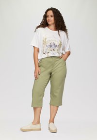 T-shirt blanc avec un design graphique multicolore, pantalon court olive, et chaussures beiges à enfiler avec une semelle en jute.