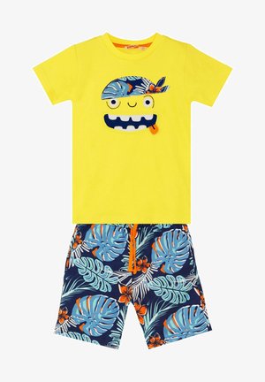 Gelbes Baumwoll-T-Shirt mit Monster-Print, kombiniert mit marineblauen Shorts, die mit tropischen Blatt- und Blumenmustern verziert sind, orangem Kordelzug.