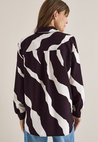 Camicia a maniche lunghe con base viola e strisce astratte bianche. Tessuto testurizzato con vestibilità rilassata e colletto classico.