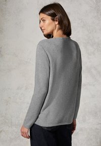 Grått stickat tröja med långa ärmar och rundad halsringning. Har en strukturerad yta och en avslappnad passform. Bärs med mörka jeans.