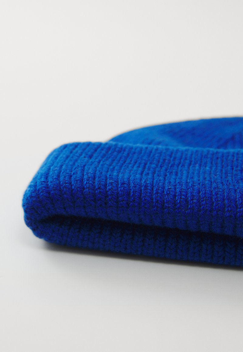 Blauwe gebreide beanie met een geribbelde textuur, voorzien van een omgeslagen rand. De stof lijkt zacht en dik, geschikt voor koude weersomstandigheden.