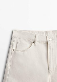 Jean en denim blanc à la taille avec une poche avant, des passants de ceinture, un bouton en métal et une petite étiquette de marque à l'intérieur de la poche.