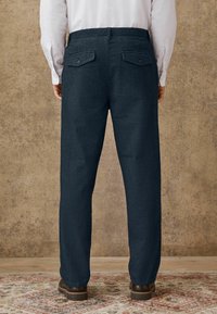 Dunkelblaue Hosen mit geradem Schnitt, aus Denim-Material. Verfügt über zwei Gesäßtaschen mit Knopfverschlüssen und einer lockeren Passform.