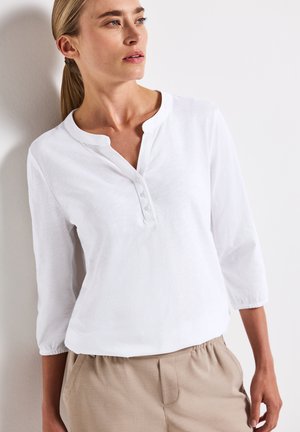 T-shirt blanc en coton à manches longues avec un col rond, une patte de boutonnage à cinq boutons et une coupe ample. Tissu texturé avec des manches légèrement froncées.