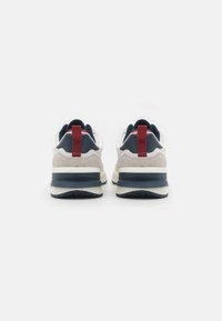 Zapatillas con una parte superior predominantemente blanca, detalles en azul marino, textura de ante, tiradores rojos en el talón y una suela gruesa en gris y blanco.