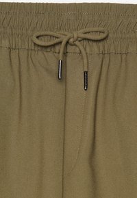 Pantaloni corti verde oliva con vita elastica, dotati di un cordoncino con aghetti argentati e tessuto liscio e strutturato.