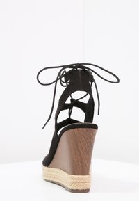 Sandal con zeppa in suede nero, caratterizzata da un tacco in legno avvolto in juta e un design con lacci alla caviglia.