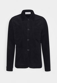 Svart kordflodjacka med krage, framknäppning med knappar och fyra fickor. Har en texturerad yta och långa ärmar.