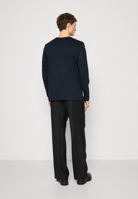 Camisa de manga larga color navy hecha de algodón, con un cuello redondo y un corte relajado, combinada con pantalones y zapatos negros.
