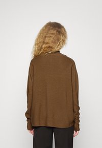 Brązowy sweter dzianinowy o luźnym kroju, z długimi rękawami, teksturowanym materiałem i okrągłym dekoltem, zaprojektowany bez wyraźnych detali czy wzorów.