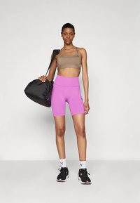 Brązowy sportowy biustonosz, różowe szorty z wysokim stanem, czarne trampki i czarna torba. Gładka tkanina, dopasowany krój i sportowy styl.