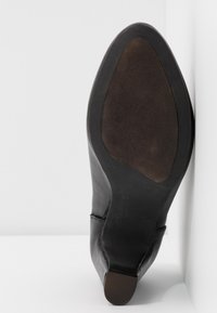 Chaussure à talon haut en cuir noir avec une texture lisse et une forme profilée, dotée d'une semelle en caoutchouc et d'une courbe subtile au niveau de l'orteil.