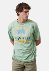 Camiseta de algodón verde menta con texto gráfico multicolor y diseño de palmera. Manga corta y estilo de cuello redondo. Corte casual.