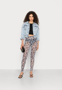 Casaco de ganga, top preto cortado, leggings estampadas com um padrão de borboleta em cinza e bege, carteira preta e sandálias de salto pretas.