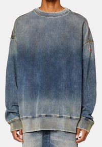 Felpa in denim con una sfumatura che va dal blu chiaro al blu scuro, vestibilità oversize, colletto a girocollo, polsini a coste e un piccolo logo sulla manica.