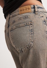 Beiga denim jeans med en texturerad yta, med bakfickor och en brun märkesläderlapp vid midjan.